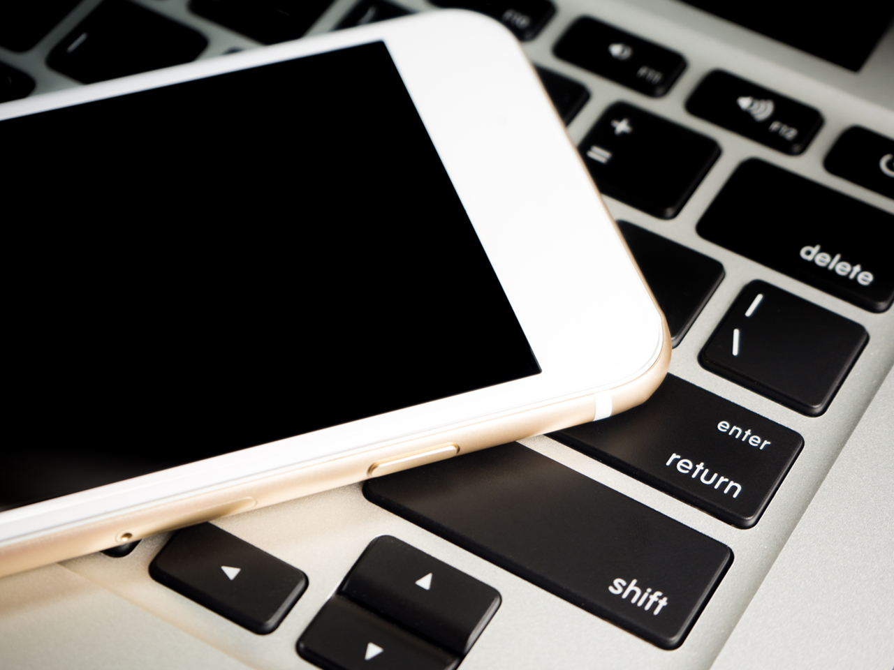 Blank White Business Smartphone on a notebook keyboard. Different modern electronics gadgets. Electronic devices (laptop and cell phone).